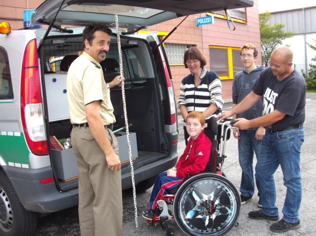 Polizeikommissar Joachim Gigli zeigt Marc Wolf (im Rollstuhl), seiner Mutter Sabine Wolf, Bruder Kevin und Vater Andreas Wolf die Ausrüstung eines Polizeieinsatzfahrzeuges