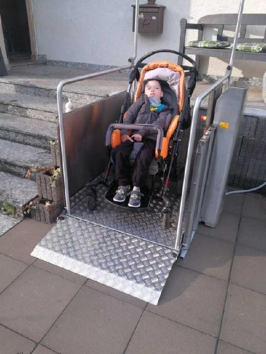 Das Foto zeigt den 9jährigen 'kleinen Kämpfer' Tim in seinem Buggy auf der am Hauseingang installierten Rollstuhl-Hebebühne, die den Alltag von Familie Haffner nun etwas erleichtert