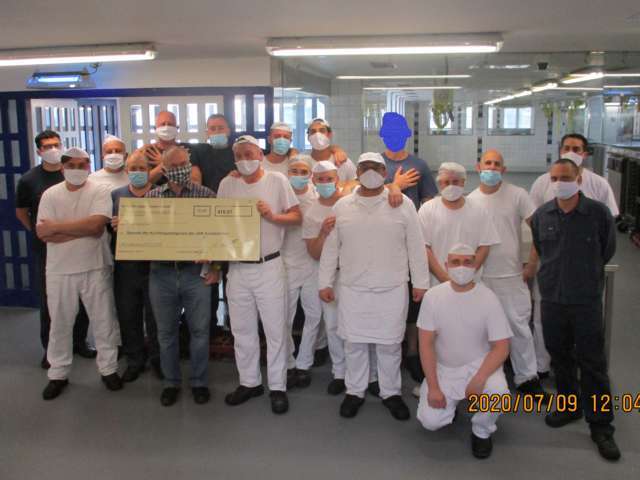Das mit Mundschutz aufgenommene Foto zeigt 18 der 23 Gefangenen, die einen kompletten Tageslohn gespendet haben, mit Klaus Port (vordere Reihe, 3. von links mit Spendenscheck) (Bildrechte: JVA Saarbrücken)